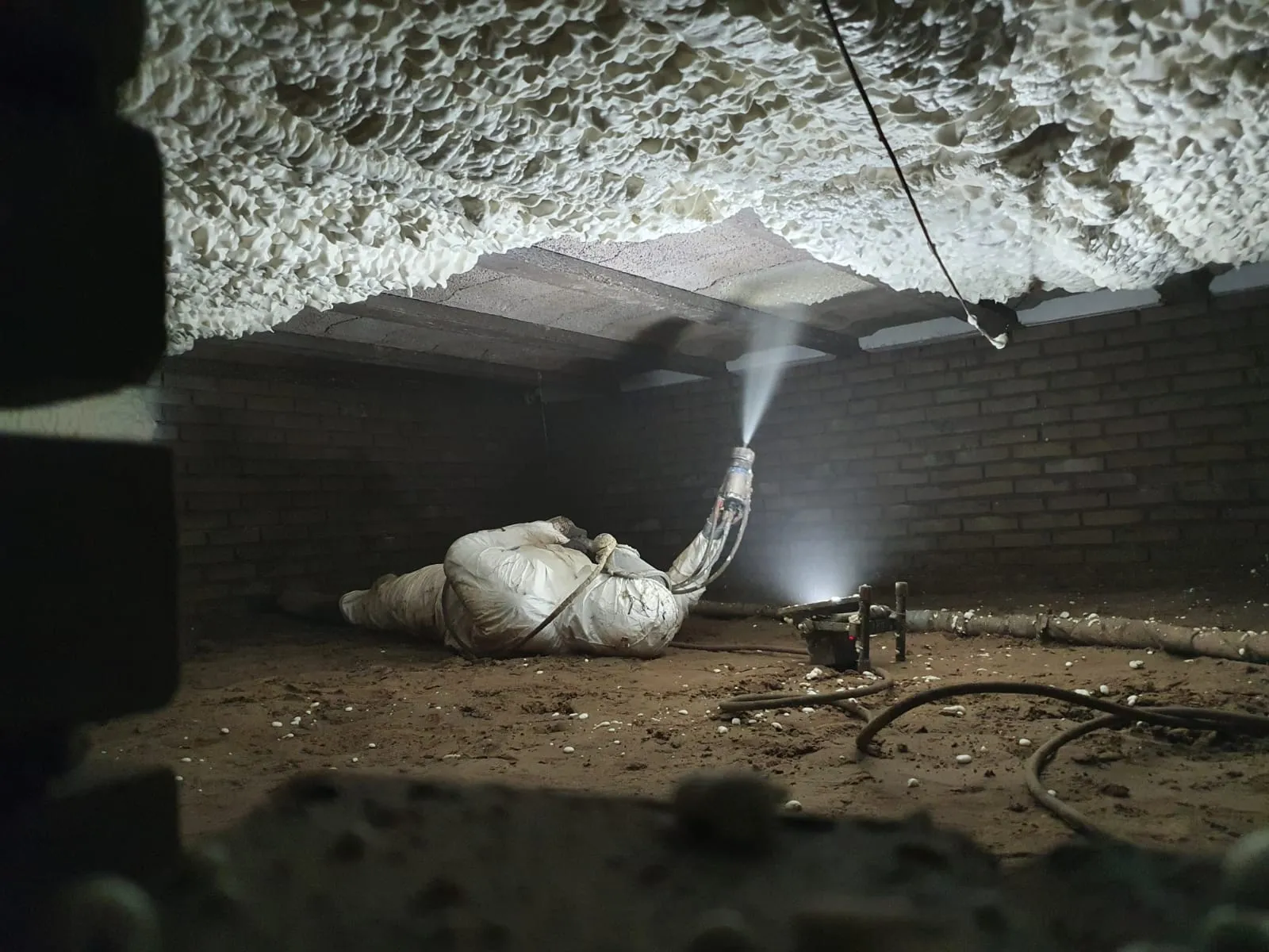 Vakman spuit liggend sprayfoam-isolatie tegen de vloer in een kruipruimte